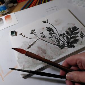 A photo of an unfinished watercolour painting of flowers, with paintbrushes held in the foreground